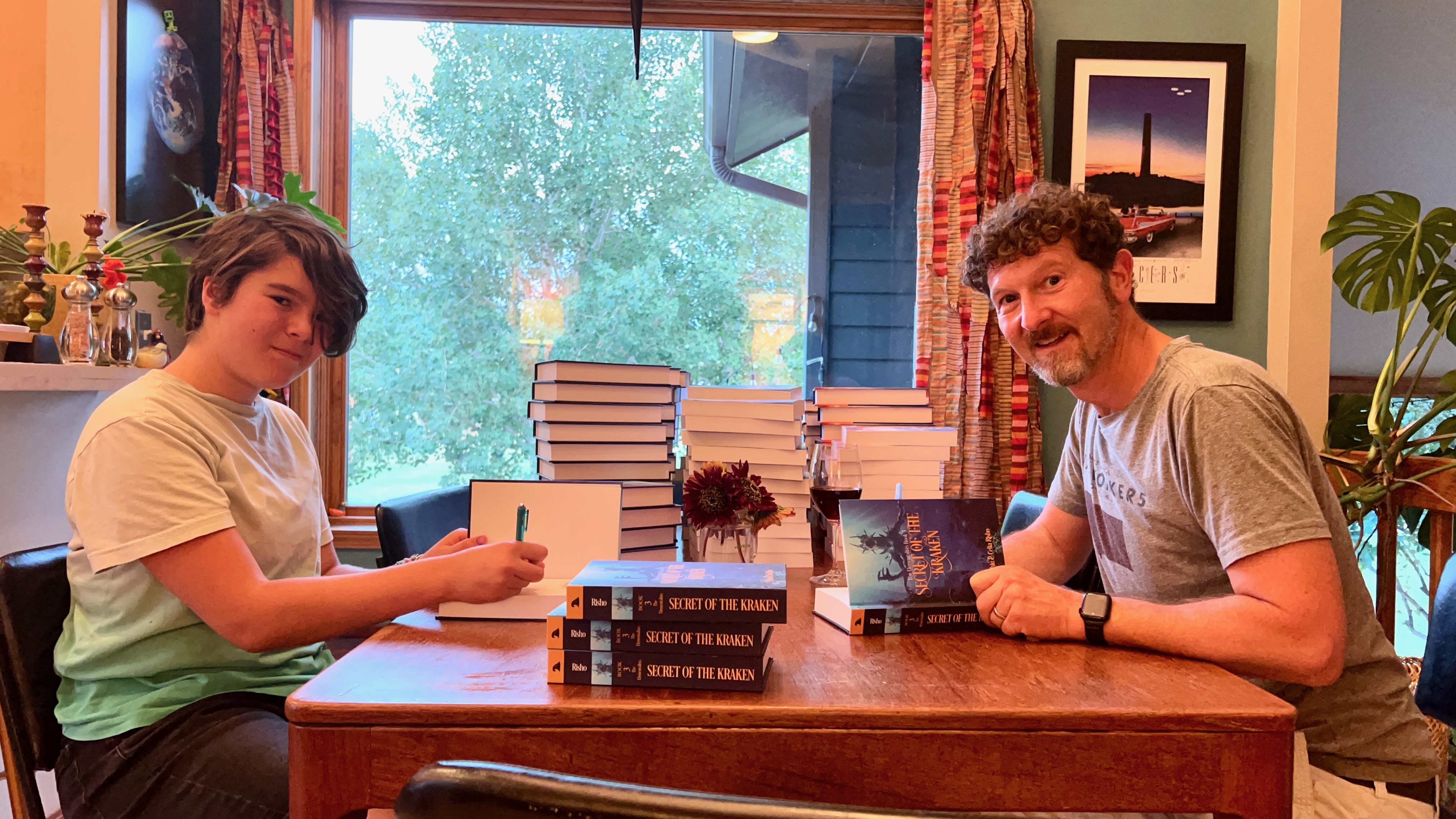 Ephie and Blue signing stacks of books at a wooden table